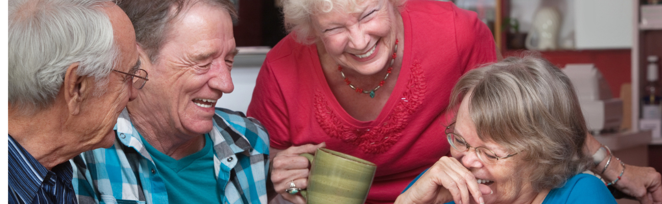 Older adults laughing at table holding coffee mugs