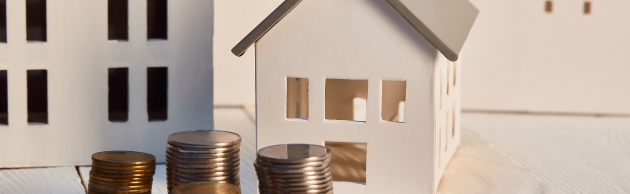 Craft wooden house with stack of coins in front of it